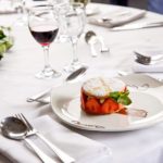 Strawberry dessert on white plate on a white table with a glass of red wine